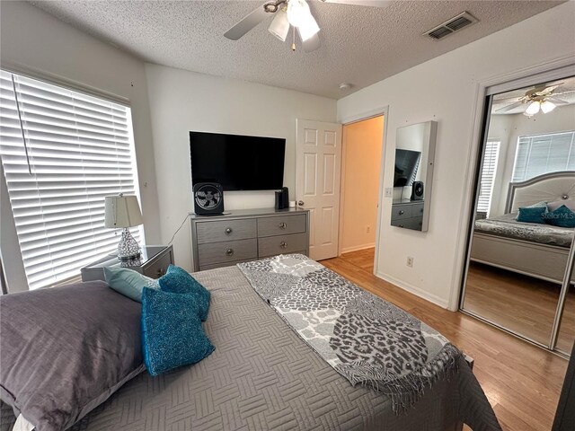 bedroom with a closet, a textured ceiling, light hardwood / wood-style floors, and ceiling fan