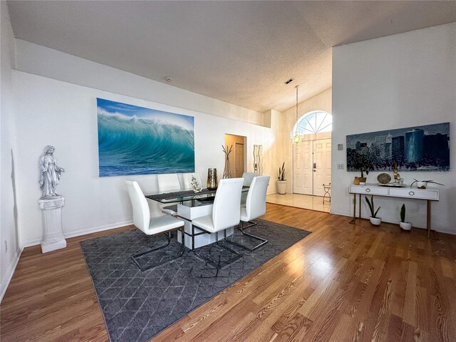 dining room featuring lofted ceiling, a chandelier, wood-type flooring, and a textured ceiling