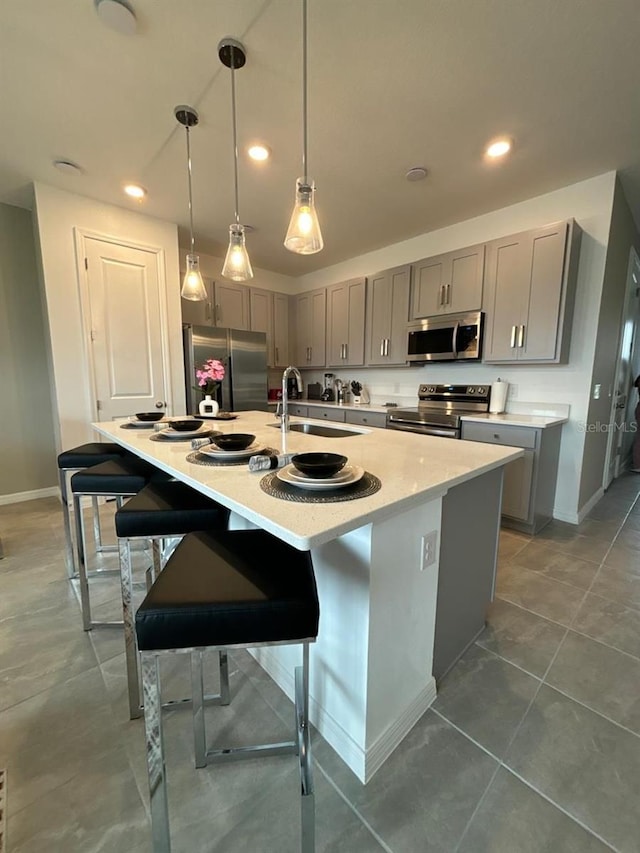 kitchen with a kitchen island with sink, gray cabinetry, pendant lighting, a breakfast bar, and stainless steel appliances