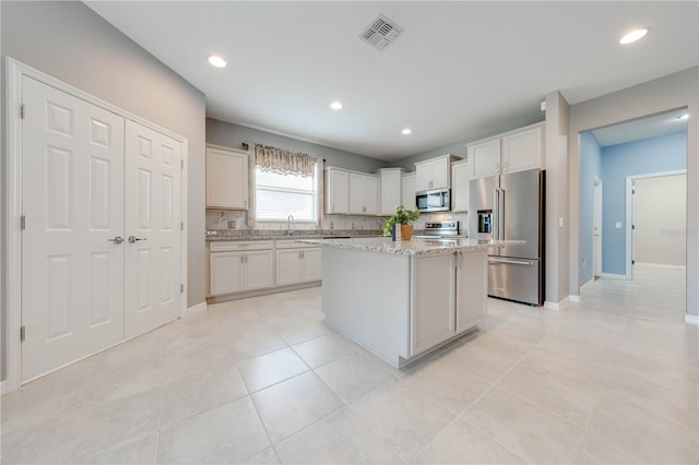 kitchen with white cabinetry, a center island, light stone countertops, tasteful backsplash, and appliances with stainless steel finishes