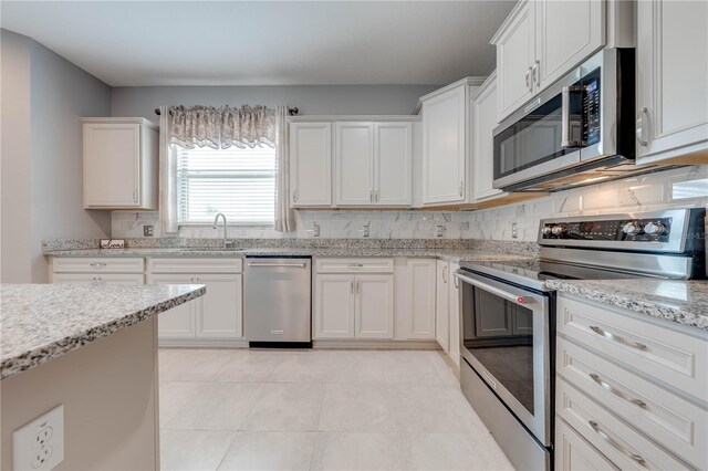 kitchen with light stone countertops, white cabinetry, sink, stainless steel appliances, and backsplash