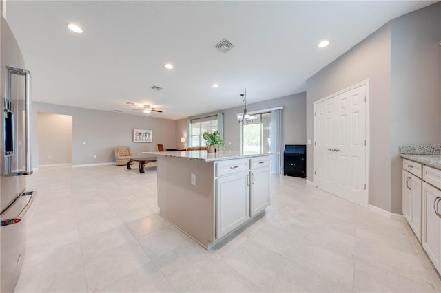 kitchen with a center island, hanging light fixtures, light stone counters, white cabinets, and ceiling fan with notable chandelier