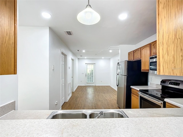 kitchen with light wood-type flooring, decorative light fixtures, stainless steel appliances, and sink