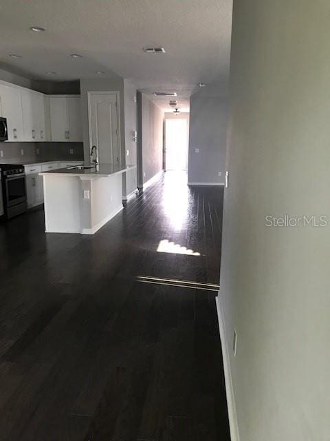 kitchen with white cabinets, stainless steel range oven, dark hardwood / wood-style flooring, sink, and a center island with sink