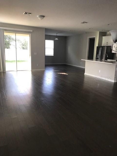 unfurnished living room featuring visible vents, baseboards, and dark wood-style flooring