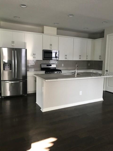 kitchen featuring an island with sink, stainless steel appliances, and white cabinets