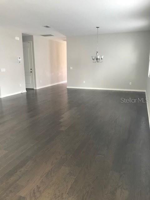 spare room with a notable chandelier, dark wood-style floors, and baseboards