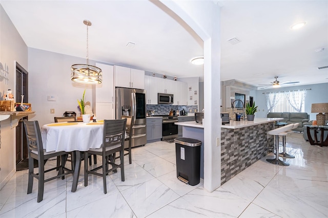 kitchen with ceiling fan with notable chandelier, decorative backsplash, hanging light fixtures, appliances with stainless steel finishes, and white cabinets