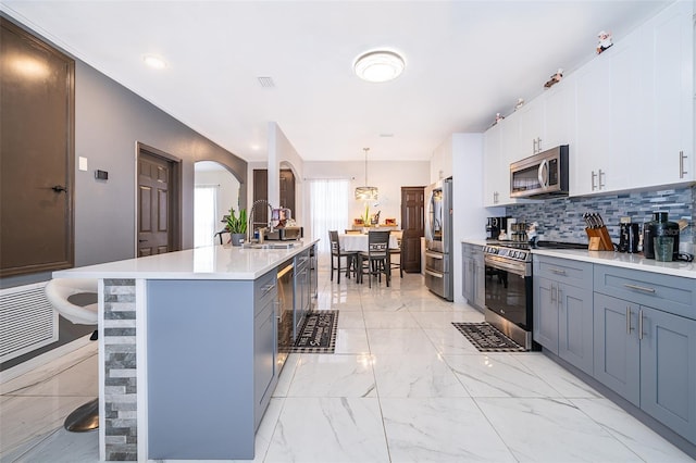 kitchen featuring stainless steel appliances, hanging light fixtures, a breakfast bar, a center island with sink, and white cabinets