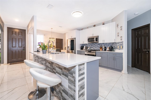 kitchen with white cabinets, backsplash, decorative light fixtures, appliances with stainless steel finishes, and a kitchen bar