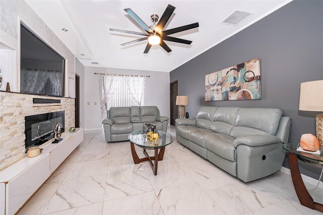 living room featuring ceiling fan, ornamental molding, and a stone fireplace