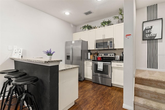 kitchen with kitchen peninsula, stainless steel appliances, white cabinetry, and a breakfast bar