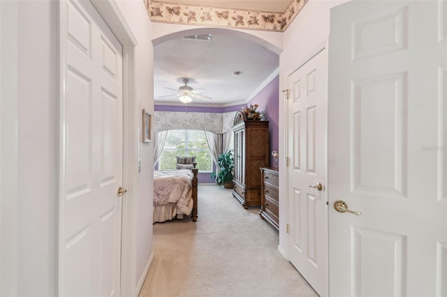 hall with light colored carpet, ornamental molding, and a textured ceiling