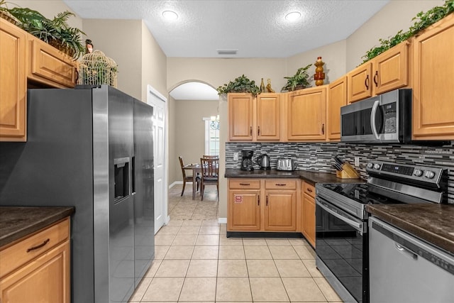 kitchen featuring backsplash, dark stone counters, light tile patterned floors, a textured ceiling, and stainless steel appliances