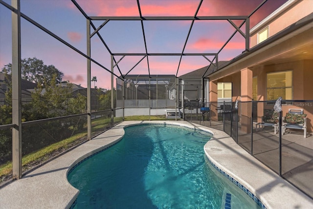 pool at dusk with glass enclosure and a patio