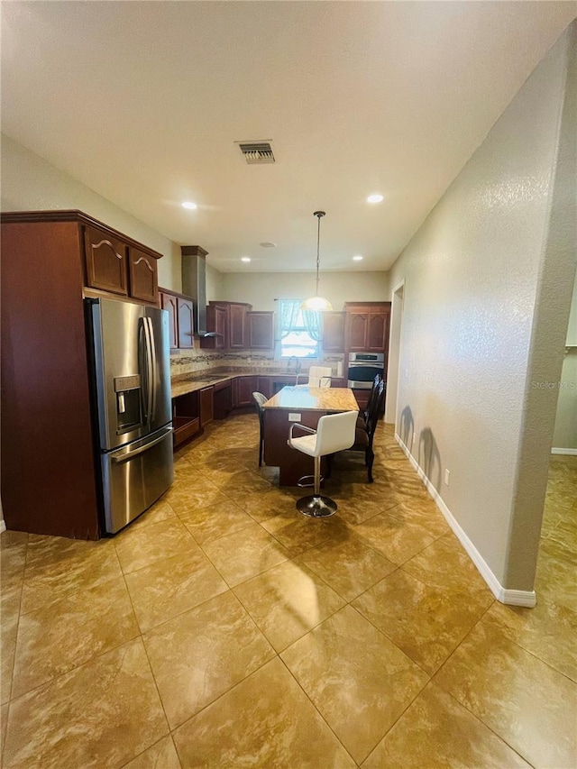 kitchen featuring decorative light fixtures, a center island, stainless steel appliances, sink, and wall chimney range hood