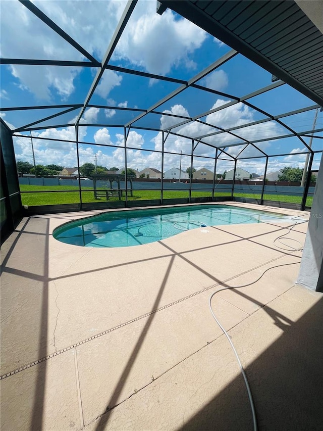 view of pool with glass enclosure, a lawn, and a patio area