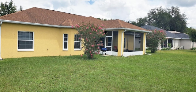 back of house with a sunroom, roof with shingles, a lawn, and stucco siding