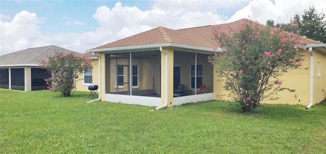 back of property featuring a garage, a sunroom, roof with shingles, and a lawn