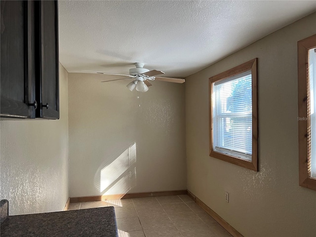 empty room with ceiling fan, light tile patterned floors, and a textured ceiling