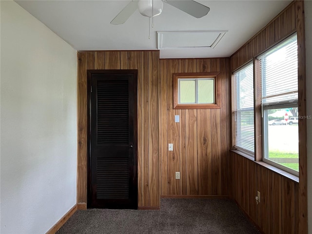 carpeted spare room with a wealth of natural light, wooden walls, and ceiling fan