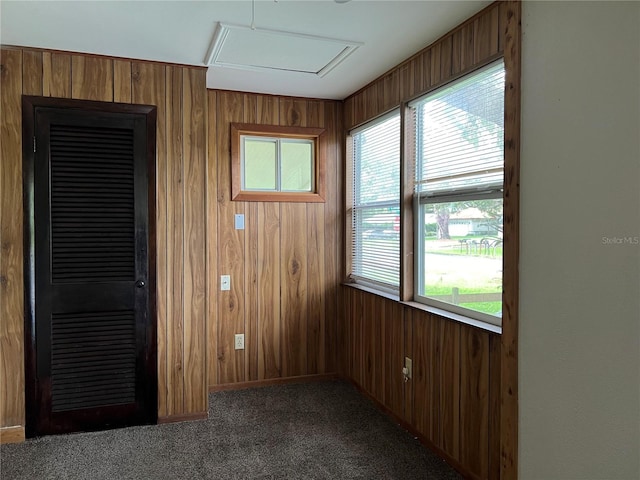 unfurnished room with wooden walls, a healthy amount of sunlight, and dark colored carpet