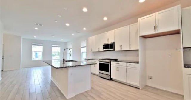 kitchen featuring white cabinets, light wood-type flooring, appliances with stainless steel finishes, sink, and a kitchen island with sink