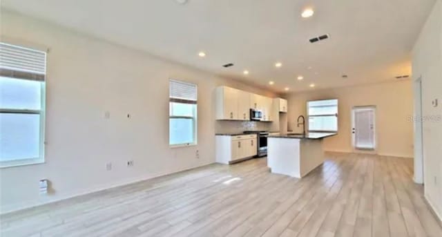 kitchen featuring a center island with sink, stainless steel appliances, light wood-type flooring, and white cabinets