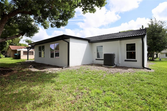 rear view of house featuring central AC unit and a lawn