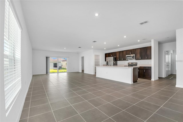 kitchen featuring an island with sink, sink, tile patterned flooring, dark brown cabinetry, and stainless steel appliances