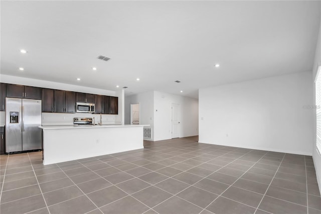 kitchen featuring a kitchen island with sink, light tile patterned floors, dark brown cabinetry, and appliances with stainless steel finishes