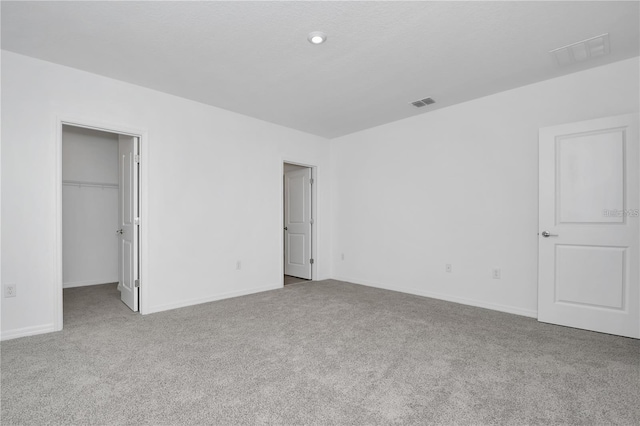 unfurnished bedroom with a closet, a spacious closet, and light carpet