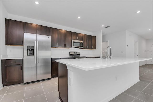 kitchen featuring stainless steel appliances, a kitchen island with sink, dark brown cabinets, and light tile patterned floors