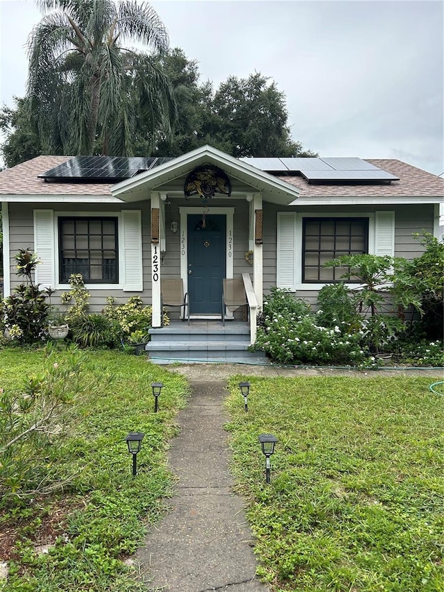 single story home featuring a porch, a front lawn, and solar panels