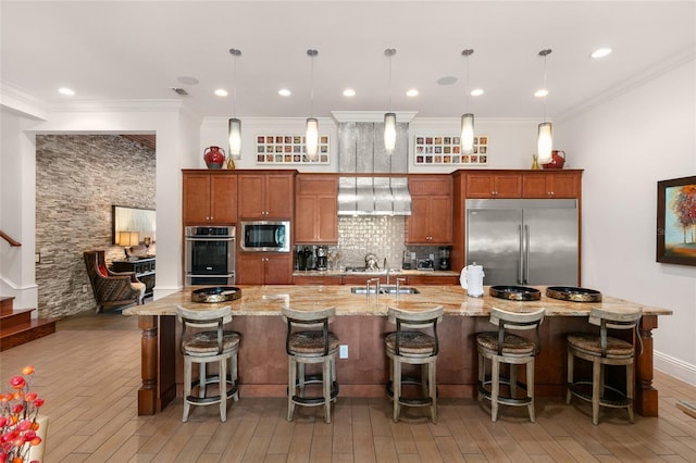 kitchen with a kitchen breakfast bar, built in appliances, decorative light fixtures, and wall chimney range hood