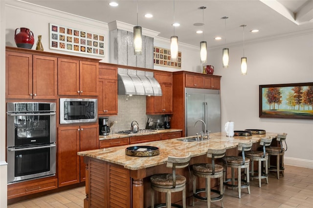 kitchen featuring a kitchen breakfast bar, wall chimney exhaust hood, a kitchen island with sink, sink, and built in appliances