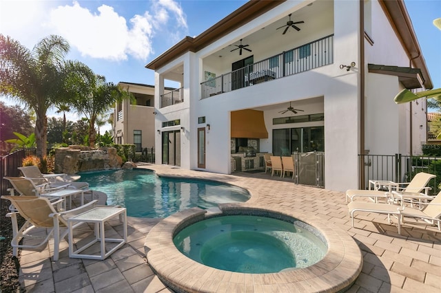 rear view of house featuring a swimming pool with hot tub, a balcony, a patio, and exterior kitchen