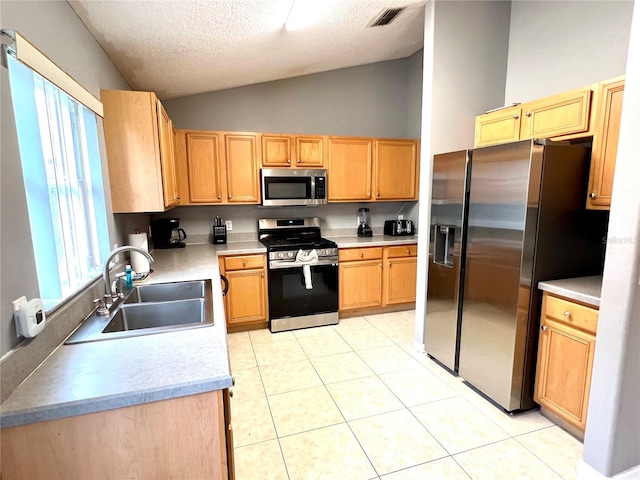 kitchen with a textured ceiling, sink, lofted ceiling, stainless steel appliances, and light tile patterned floors