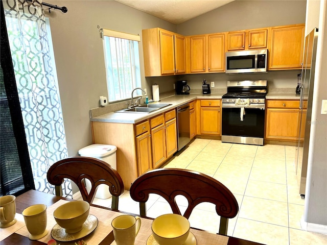 kitchen with stainless steel appliances, lofted ceiling, light tile patterned floors, and sink