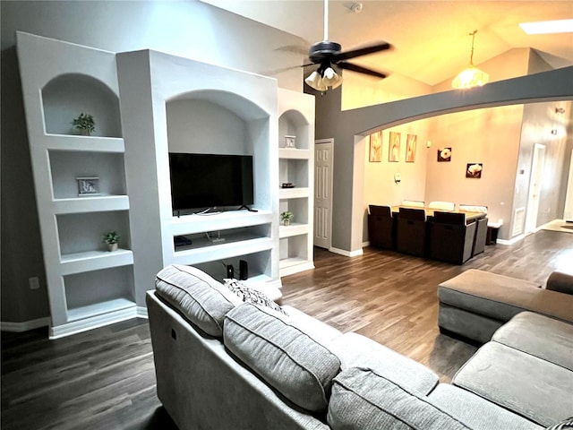 living room with built in shelves, vaulted ceiling, ceiling fan, and dark wood-type flooring