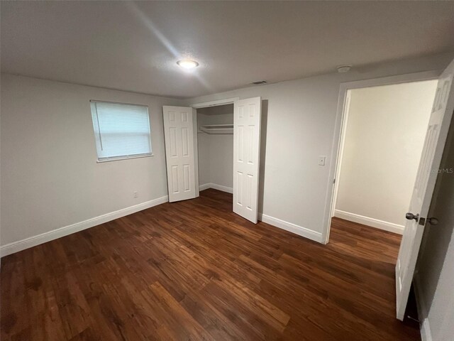 unfurnished bedroom with dark wood finished floors, visible vents, a closet, and baseboards