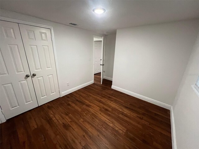 unfurnished bedroom featuring visible vents, baseboards, a closet, and dark wood finished floors