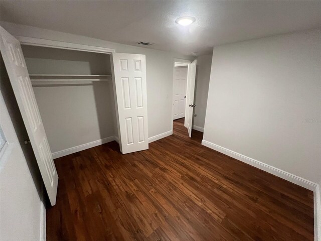 unfurnished bedroom featuring dark wood-style floors, visible vents, a closet, and baseboards