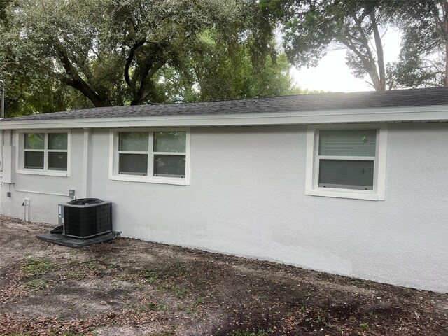 view of side of property featuring central air condition unit, a shingled roof, and stucco siding