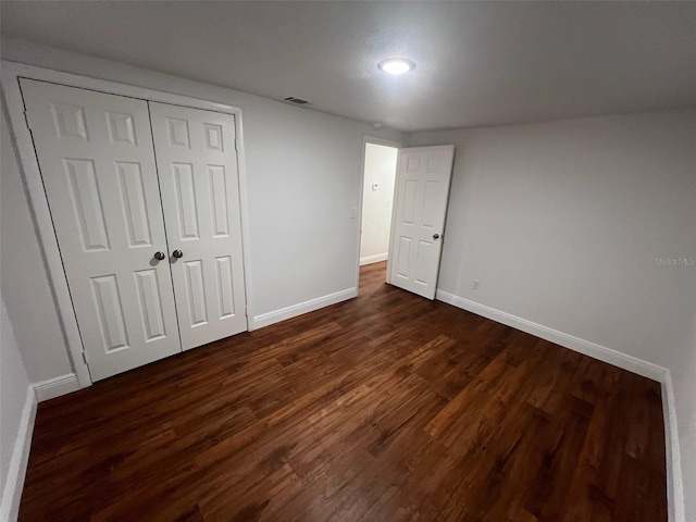 unfurnished bedroom with dark wood-type flooring, baseboards, visible vents, and a closet