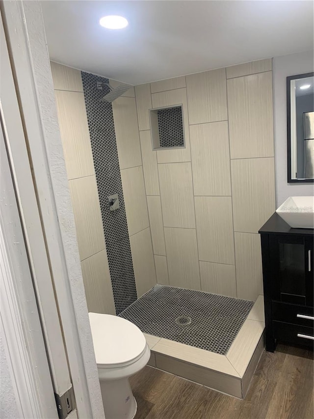 bathroom featuring visible vents, toilet, wood finished floors, tiled shower, and vanity