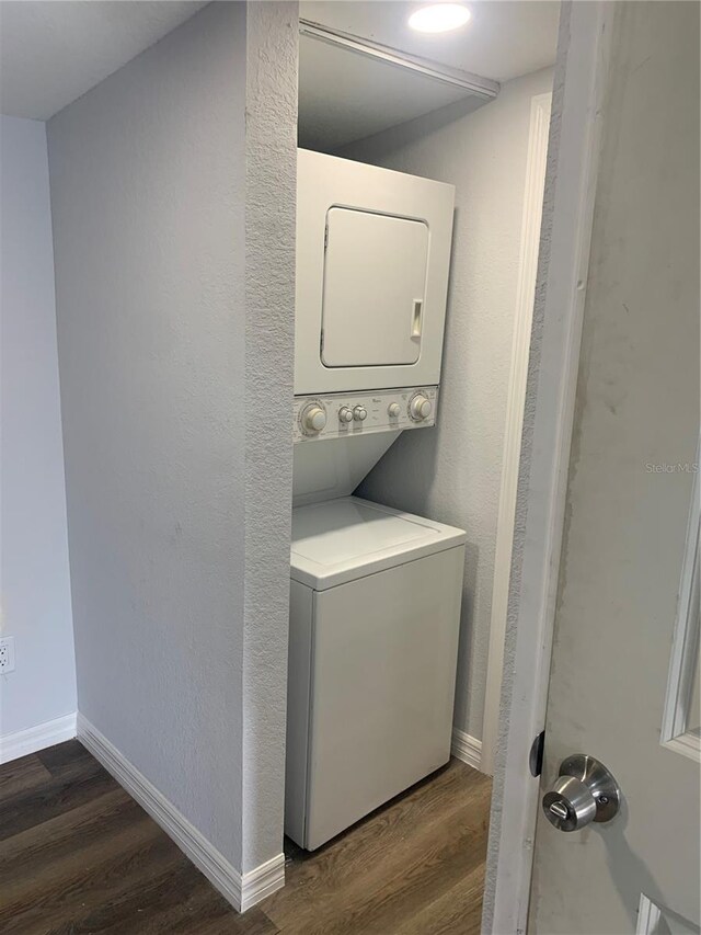 laundry area with dark wood-type flooring and stacked washer / dryer