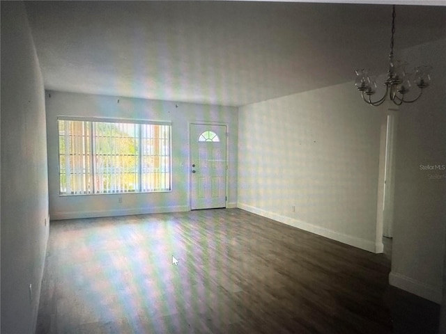 empty room featuring dark wood-type flooring and an inviting chandelier