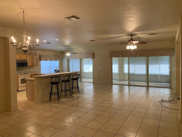 kitchen featuring a kitchen breakfast bar, ceiling fan with notable chandelier, light brown cabinetry, light tile patterned floors, and white electric range