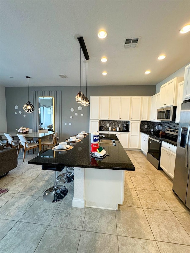 kitchen with pendant lighting, light tile patterned floors, appliances with stainless steel finishes, an island with sink, and white cabinets